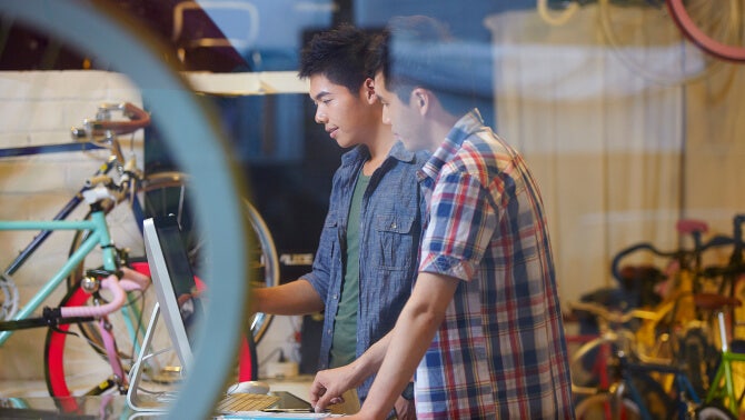 Two people examining batch bicycles from a storefront bike shop window